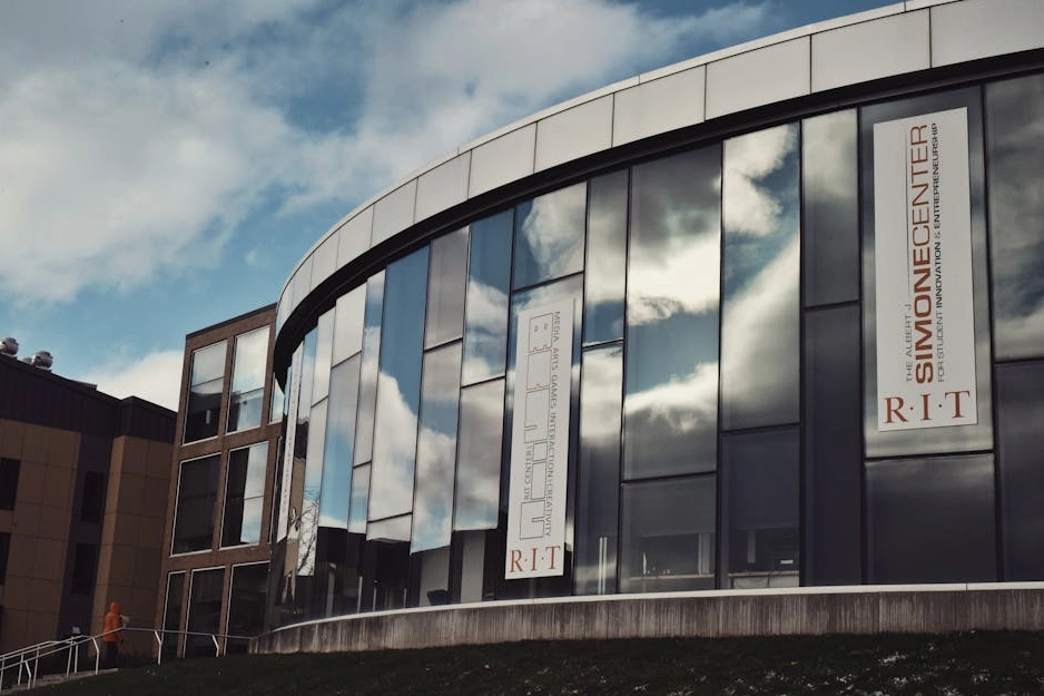 Moderno edificio universitario con ampie vetrate che riflettono il cielo.